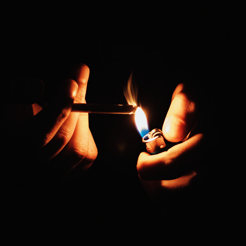 An image of two hands in a dark background lighting a cigarette